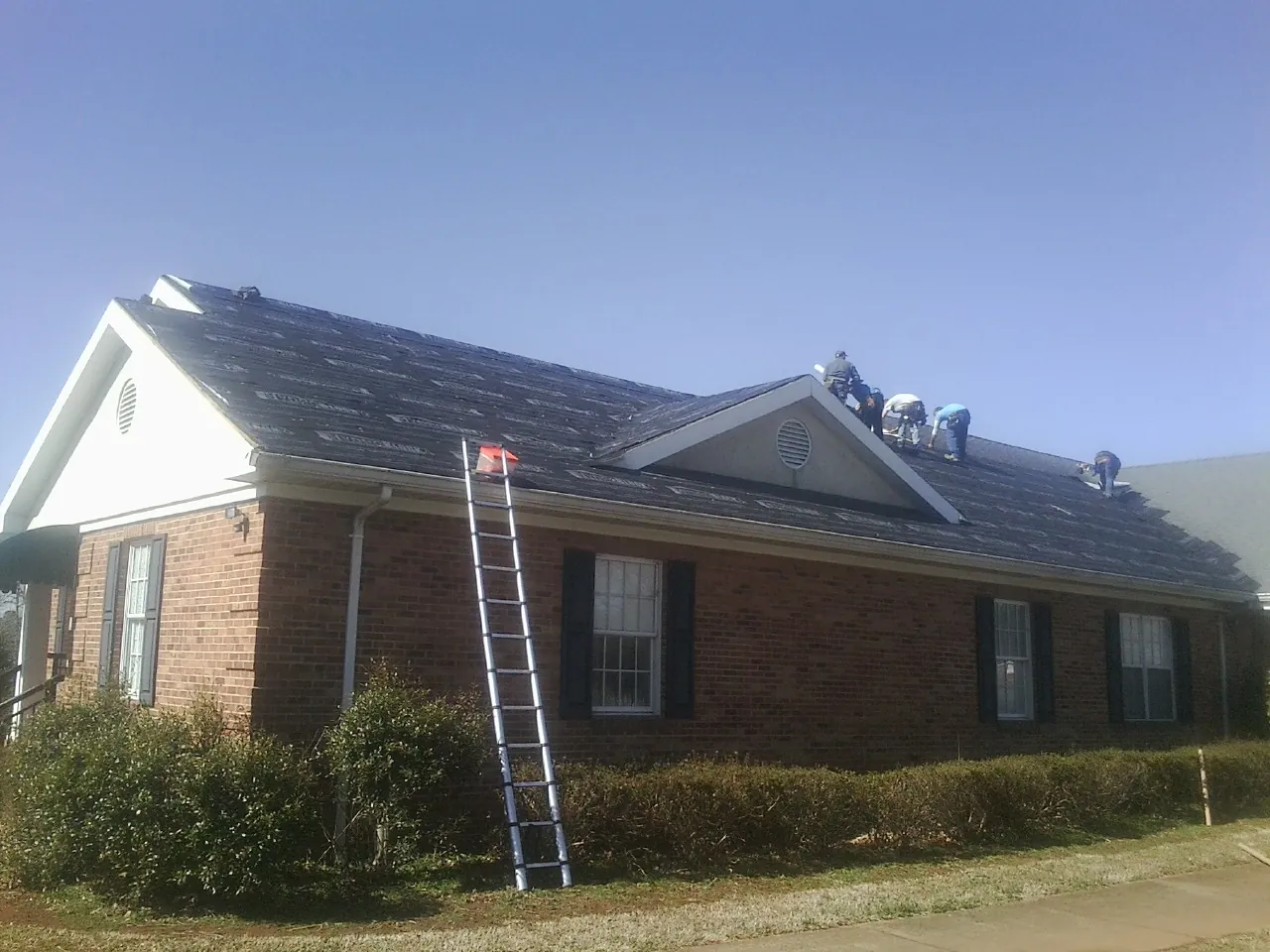 Crew tearing shingles off a brick ranch roof with a ladder set — Emergency Roof Repair work by our crew in Conesville