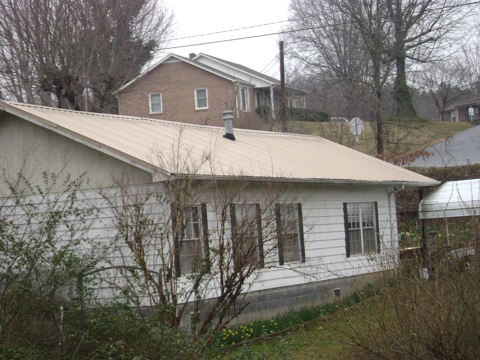 Tan metal roof on a white sided house set into a hillside — Commercial Roofing by Roofing Brothers in Conesville