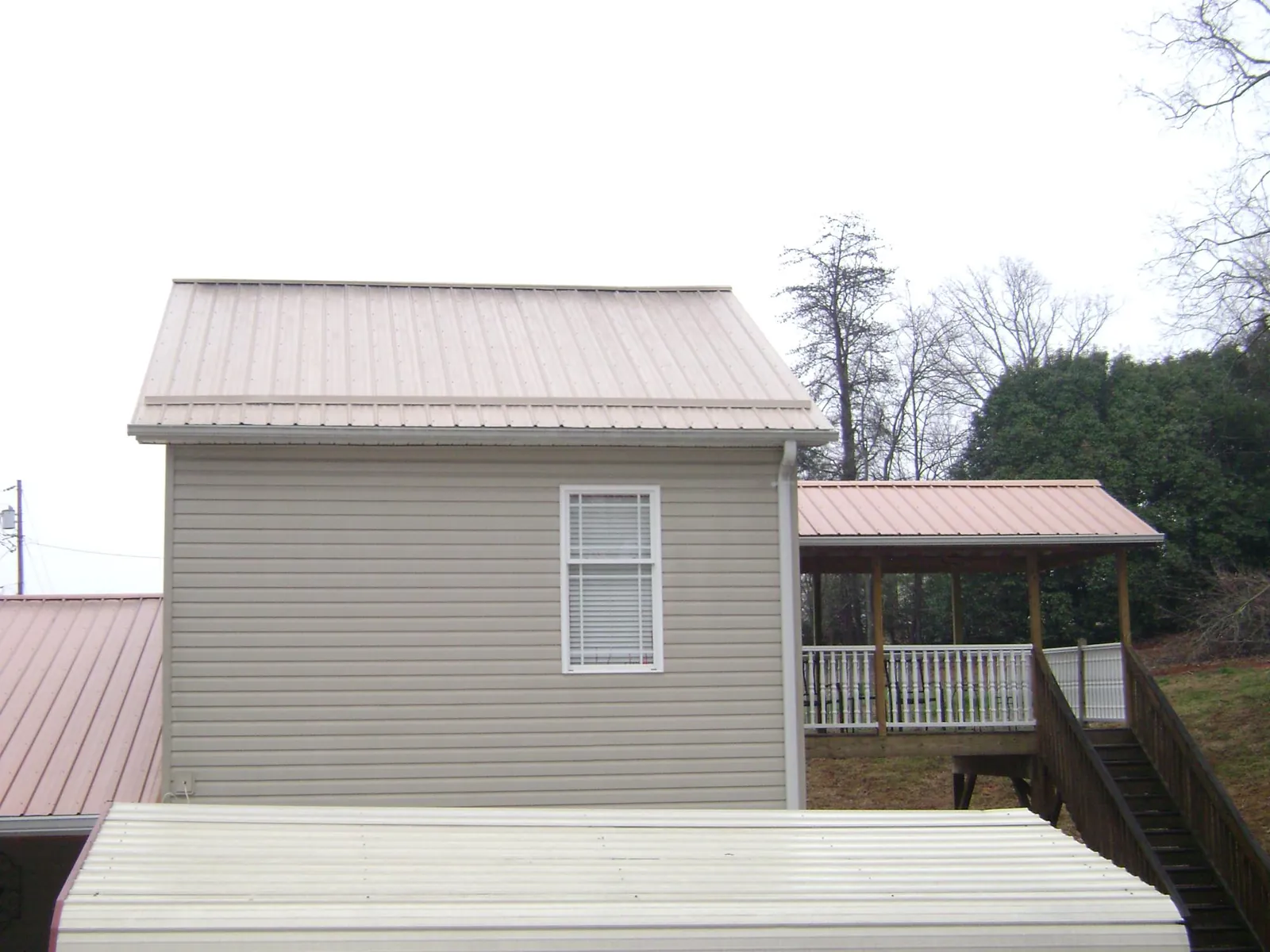 Tan metal roofs on a two story addition and attached porch, from a Roof Replacement job in Conesville